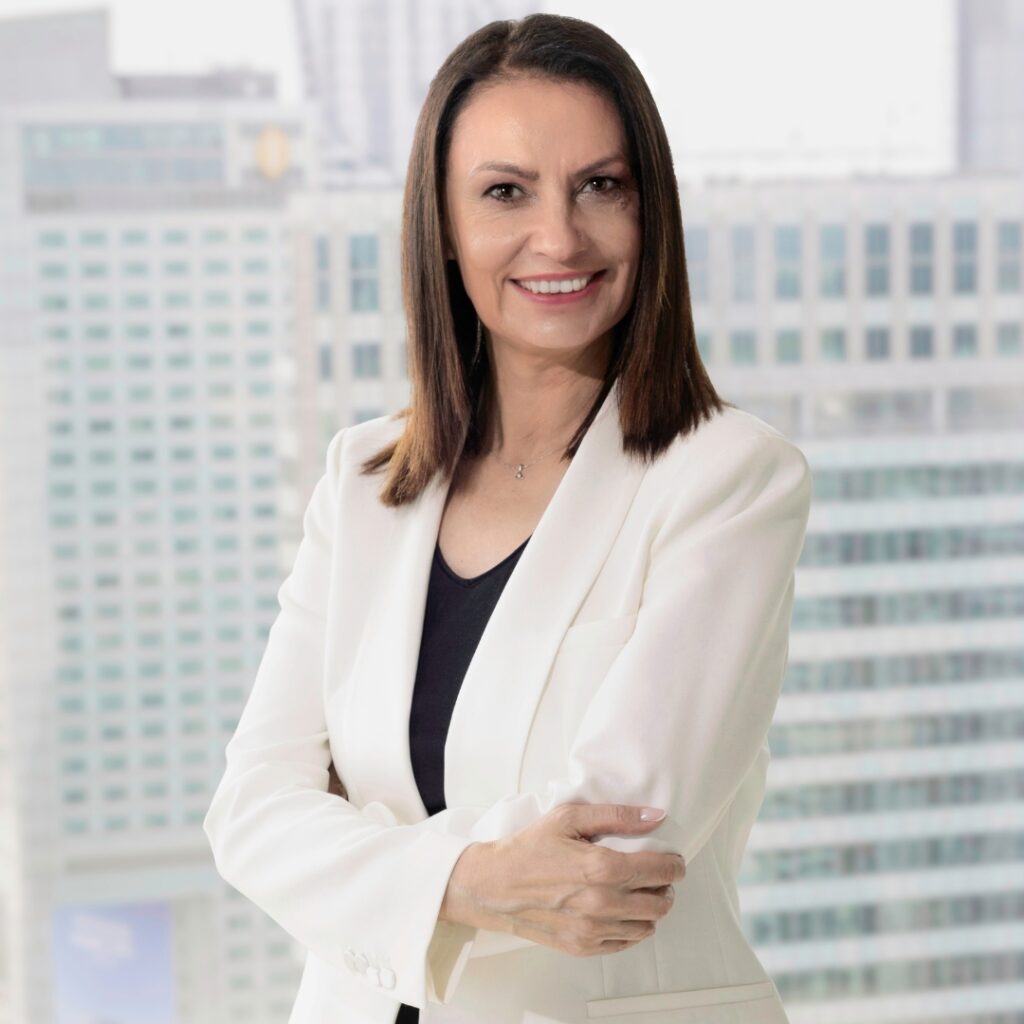 Urszula Uchańska w białej marynarce na tle nowoczesnego biurowca.